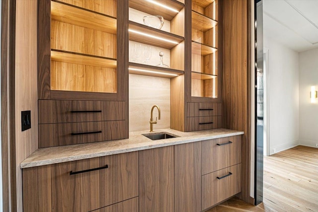 bar featuring a sink, indoor wet bar, baseboards, decorative backsplash, and wood finished floors
