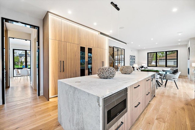 kitchen with light stone counters, light brown cabinets, stainless steel microwave, a spacious island, and modern cabinets