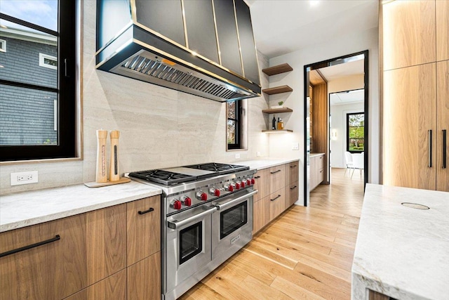kitchen featuring open shelves, decorative backsplash, wall chimney range hood, light wood-type flooring, and range with two ovens