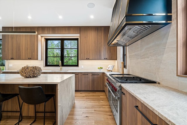 kitchen with decorative backsplash, wall chimney exhaust hood, high end stainless steel range, and a kitchen bar
