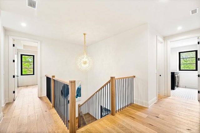 hall featuring visible vents, an inviting chandelier, light wood-style floors, washer and clothes dryer, and an upstairs landing