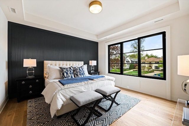 bedroom with an accent wall, a tray ceiling, visible vents, and light wood finished floors