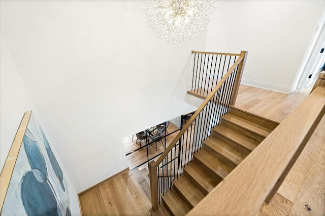 stairs featuring an inviting chandelier, baseboards, and wood finished floors
