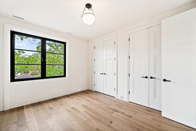 unfurnished bedroom with baseboards, multiple closets, light wood-style flooring, and visible vents