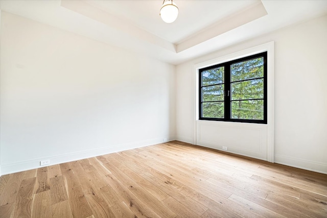 empty room featuring light wood-type flooring, baseboards, and a tray ceiling