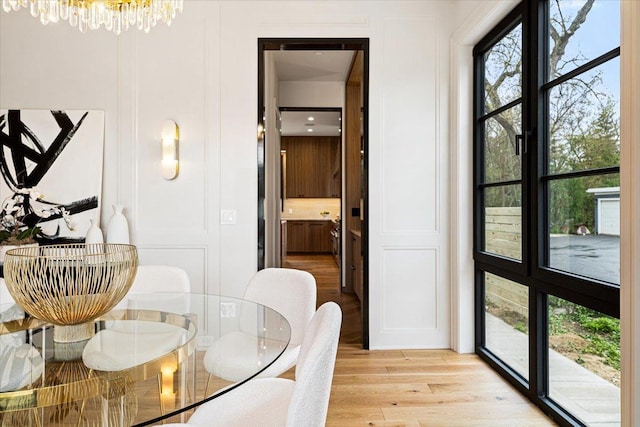 dining room featuring a chandelier, light wood-type flooring, a wealth of natural light, and a decorative wall