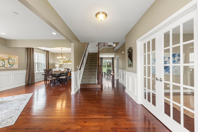 foyer entrance featuring wainscoting, a decorative wall, french doors, stairs, and dark wood-style floors