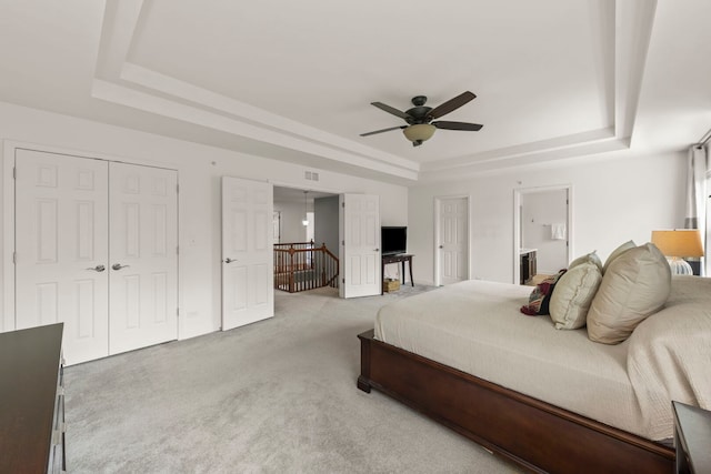 bedroom featuring ceiling fan, visible vents, a closet, light carpet, and a tray ceiling