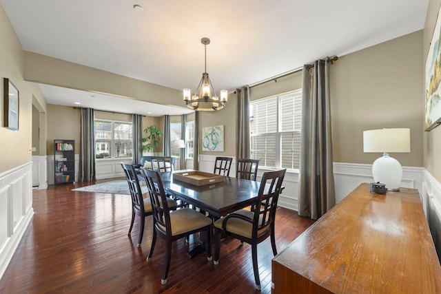 dining area with dark wood-style floors, a notable chandelier, wainscoting, and a decorative wall