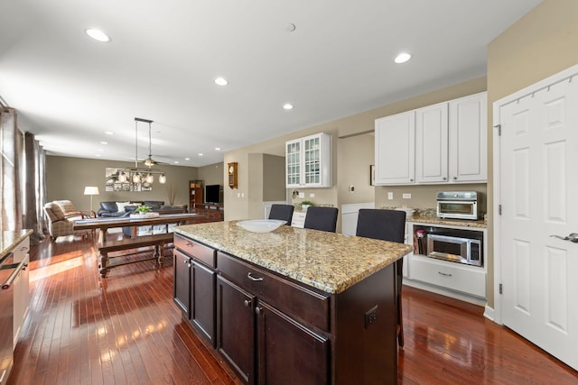 kitchen featuring light stone counters, stainless steel microwave, open floor plan, white cabinetry, and dark wood-type flooring