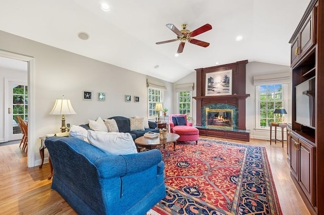 living room featuring vaulted ceiling, light wood finished floors, a wealth of natural light, and a high end fireplace