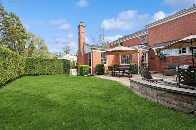 back of property featuring a lawn, a patio area, a chimney, and brick siding