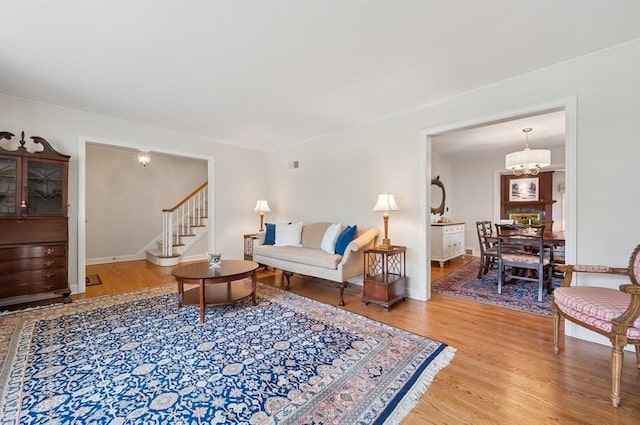 living area with an inviting chandelier, light wood-style flooring, and stairs