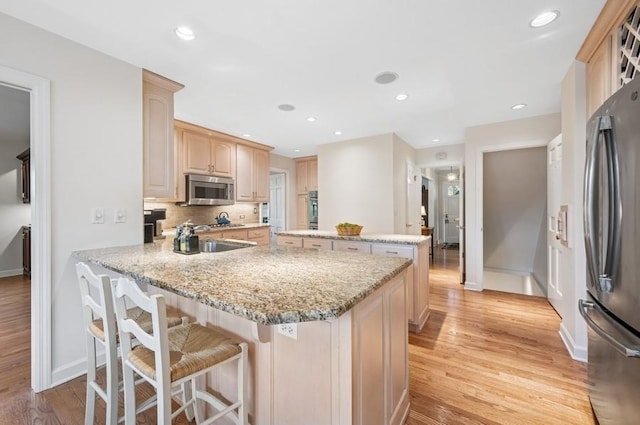kitchen with a peninsula, stainless steel appliances, light brown cabinets, light wood-type flooring, and baseboards