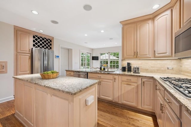 kitchen featuring light wood finished floors, a peninsula, a sink, light brown cabinetry, and stainless steel appliances