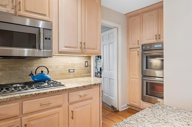 kitchen with light brown cabinets, decorative backsplash, light wood-type flooring, and appliances with stainless steel finishes
