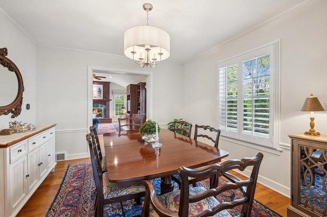 dining space with baseboards, visible vents, a chandelier, crown molding, and wood finished floors