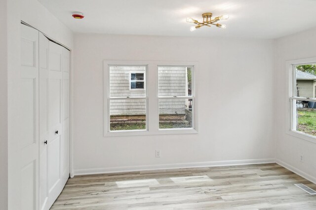 unfurnished bedroom featuring light wood-style floors, a closet, visible vents, and multiple windows