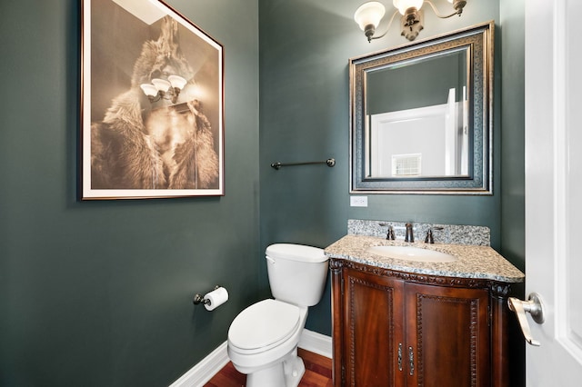 half bathroom with a chandelier, toilet, vanity, wood finished floors, and baseboards