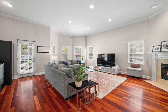 living room featuring a tiled fireplace, dark wood-type flooring, ornamental molding, recessed lighting, and baseboards