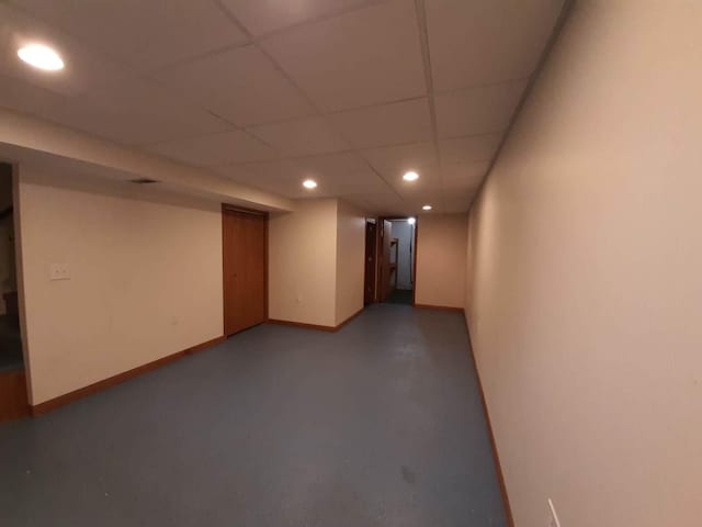 finished below grade area featuring a paneled ceiling, baseboards, and recessed lighting