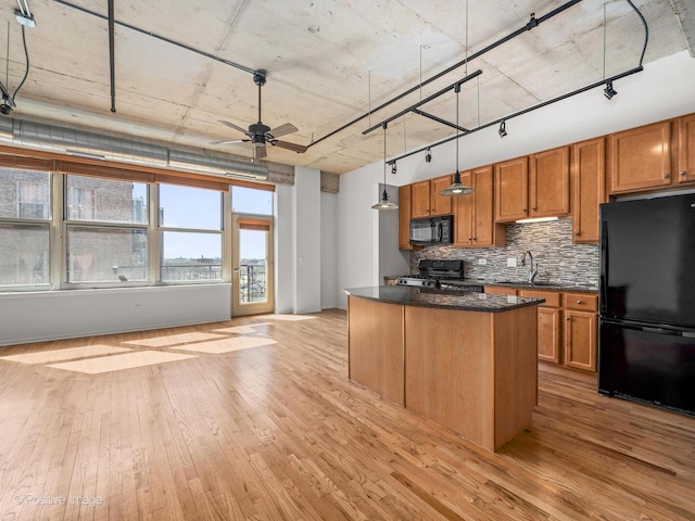 kitchen featuring dark countertops, light wood-type flooring, a center island, tasteful backsplash, and black appliances