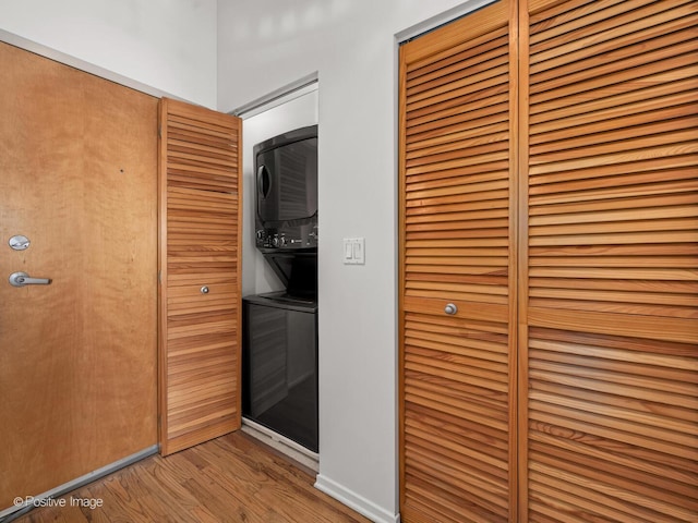 laundry room featuring laundry area, stacked washer / drying machine, and wood finished floors