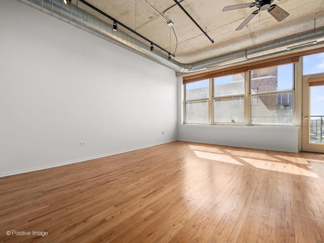 empty room with plenty of natural light, wood-type flooring, and rail lighting