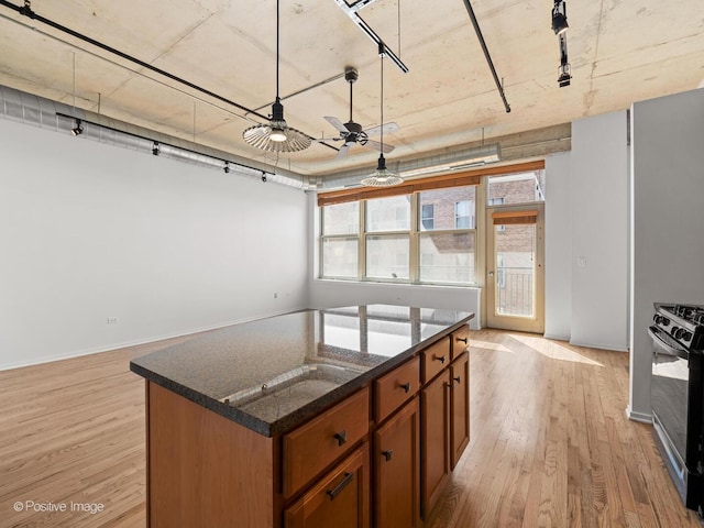 kitchen with range with gas cooktop, a ceiling fan, a center island, light wood-style floors, and dark stone counters