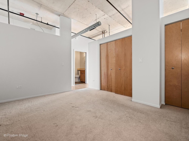 unfurnished bedroom with carpet floors, baseboards, and two closets