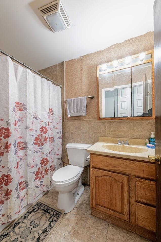 bathroom with visible vents, tile walls, curtained shower, vanity, and toilet