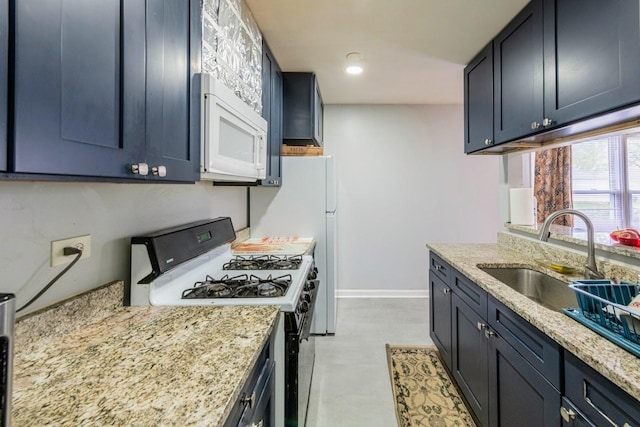 kitchen with light stone countertops, a sink, baseboards, white microwave, and gas range oven
