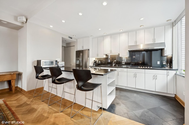 kitchen featuring under cabinet range hood, baseboards, appliances with stainless steel finishes, and dark countertops