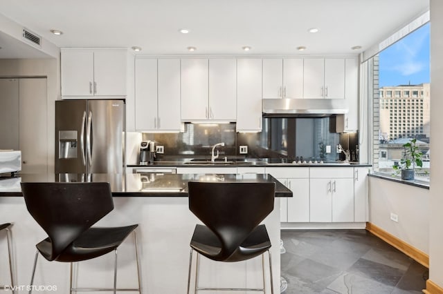 kitchen featuring white cabinets, a breakfast bar, a sink, stainless steel fridge with ice dispenser, and visible vents