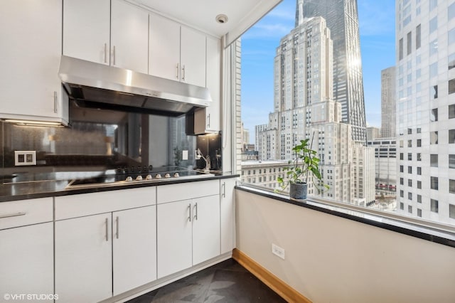 kitchen with dark countertops, a city view, black electric stovetop, under cabinet range hood, and white cabinetry
