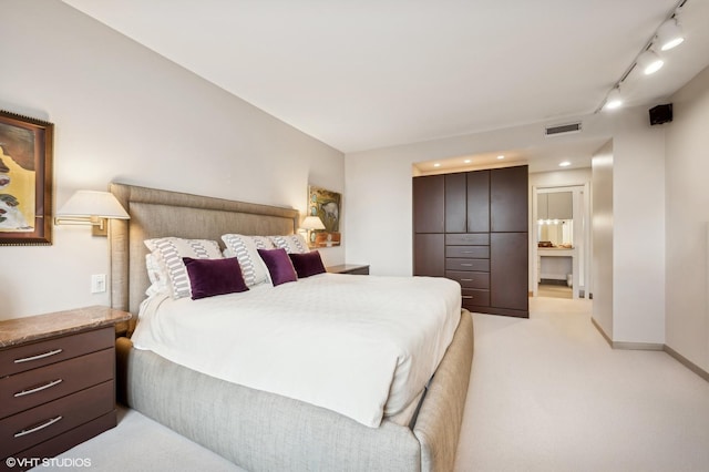 bedroom featuring visible vents, track lighting, baseboards, ensuite bathroom, and light colored carpet