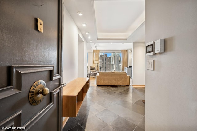 corridor featuring dark tile patterned flooring, baseboards, a tray ceiling, and recessed lighting