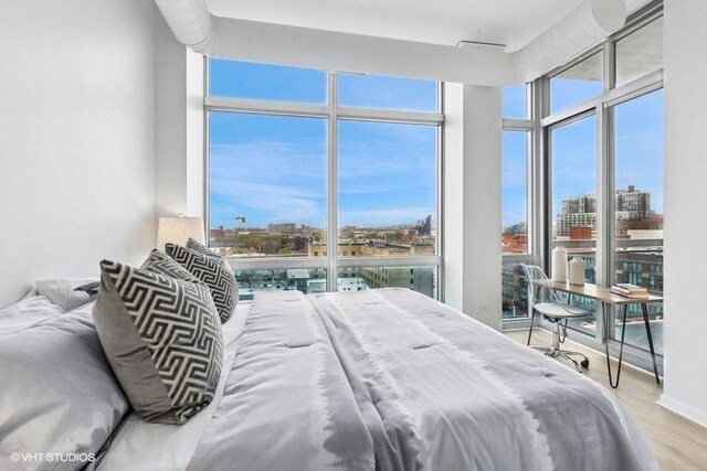 bedroom with a view of city, wood finished floors, and a wall of windows