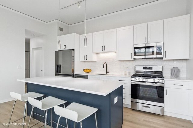 kitchen featuring a breakfast bar, a sink, light countertops, stainless steel appliances, and white cabinetry