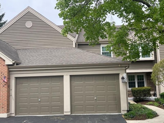 view of front of property with brick siding, an attached garage, a shingled roof, and aphalt driveway