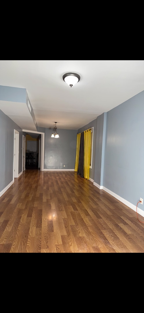 3824 W Grenshaw St, Chicago, IL 60624 - unfurnished living room with wood finished floors, baseboards, and a chandelier
