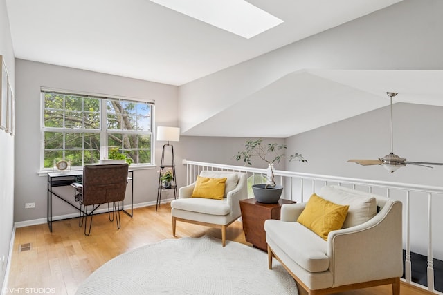 sitting room with vaulted ceiling with skylight, a ceiling fan, visible vents, light wood-type flooring, and baseboards