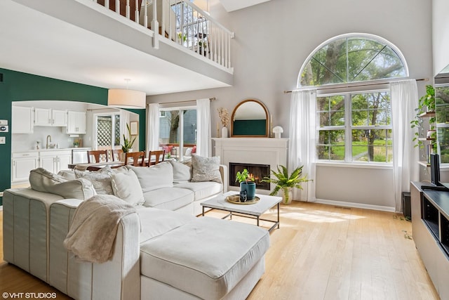 living area featuring light wood-style floors, baseboards, a warm lit fireplace, and a towering ceiling