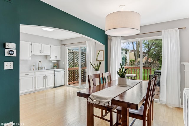dining area with arched walkways and light wood-style flooring