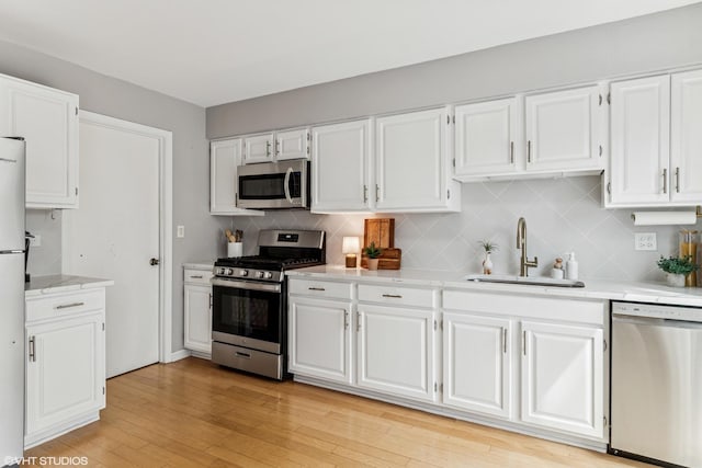 kitchen with white cabinets, a sink, light wood-style floors, stainless steel appliances, and backsplash