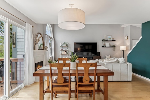 dining area with plenty of natural light, a warm lit fireplace, and light wood-style flooring