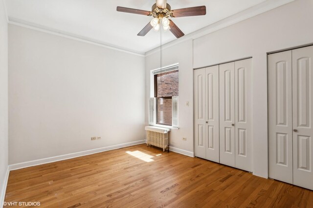 unfurnished bedroom with baseboards, multiple closets, radiator, ornamental molding, and light wood-style flooring