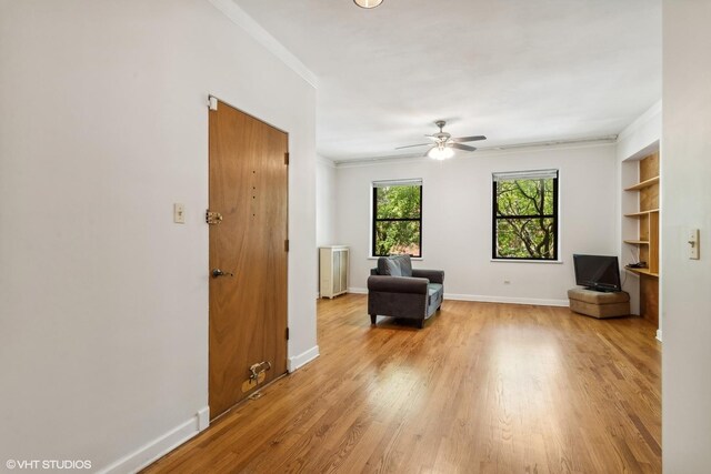living area featuring a ceiling fan, baseboards, ornamental molding, and light wood finished floors