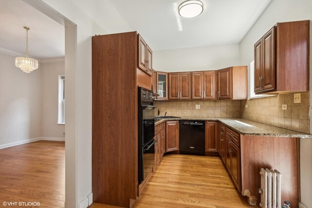 kitchen featuring radiator, stone countertops, a chandelier, light wood-style flooring, and black appliances