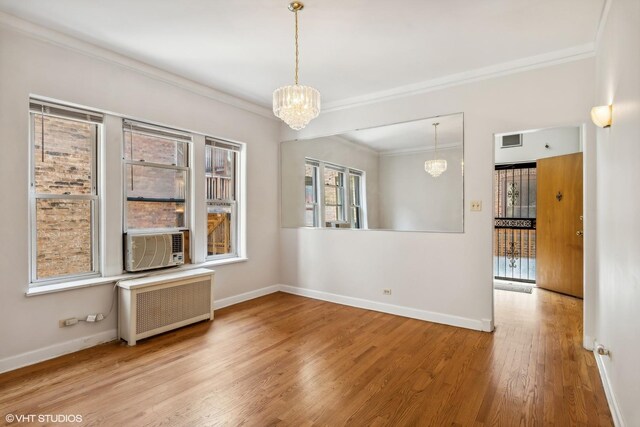 spare room featuring a notable chandelier, radiator, wood finished floors, visible vents, and ornamental molding